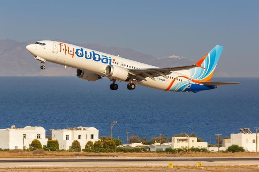 avión de flydubai volando a baja altitud, con pequeñas casas blancas y el mar al fondo.