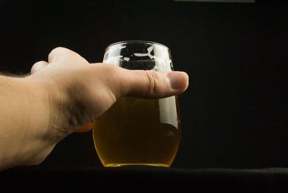 Una mano sosteniendo un vaso de cerveza, solo visibles la mano y el vaso.