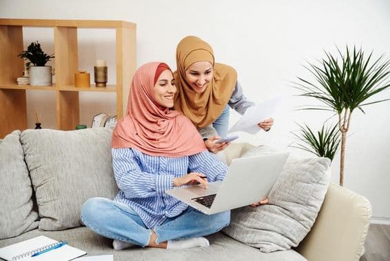 Dos mujeres emiratíes revisando un contrato y un cuaderno, una sosteniendo un teléfono, sentadas en un sofá.