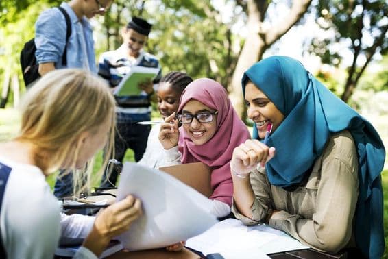 Estudiantes en Dubái escribiendo lecciones y conversando al aire libre.