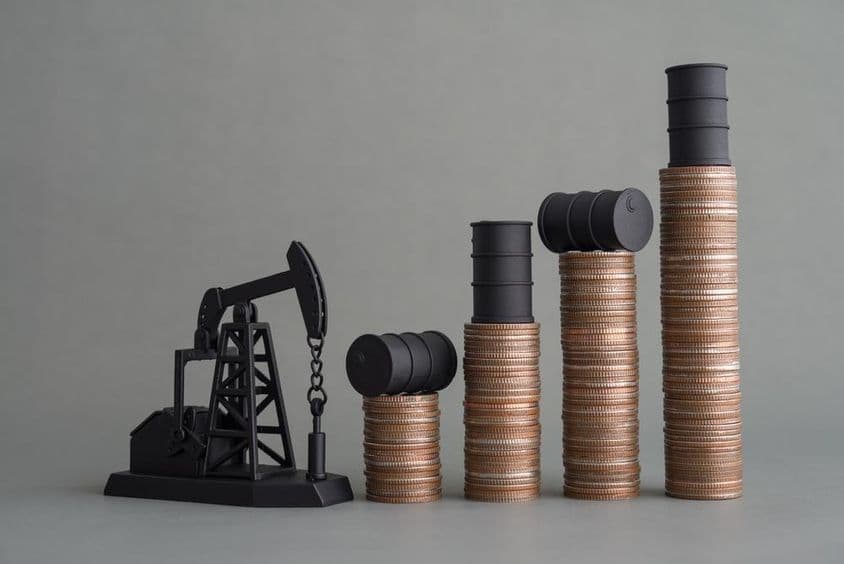 Mini plataforma petrolera y monedas apiladas con un barril de petróleo en la parte superior.