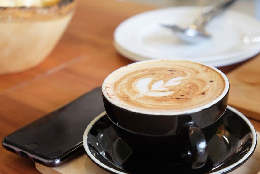 Una taza de capuchino sobre una mesa con un teléfono al lado.