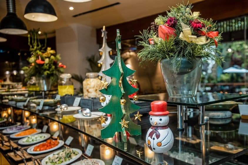 Pequeño muñeco de nieve en un restaurante sobre un mostrador de vegetales, junto a un árbol de Navidad de madera.
