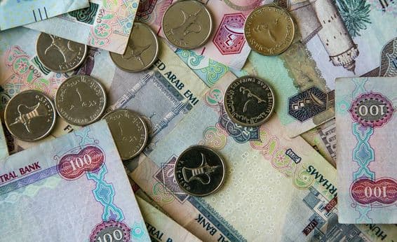 Moneda de papel de Dubái esparcida sobre una mesa con monedas de 1 dirham encima.