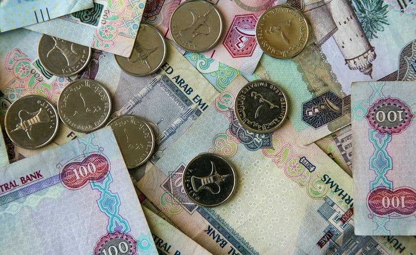 Moneda de papel de Dubái esparcida sobre una mesa con monedas de 1 dirham encima.
