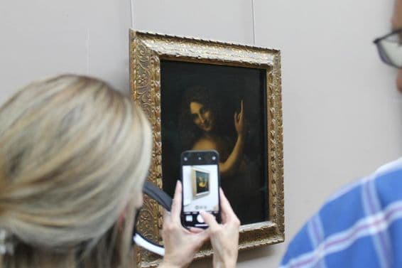 La pintura de San Juan Bautista en una pared, con una mujer tomando una foto de ella con un teléfono.
