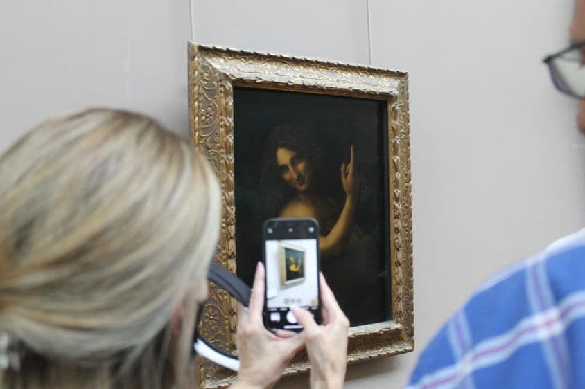 La pintura de San Juan Bautista en una pared, con una mujer tomando una foto de ella con un teléfono.