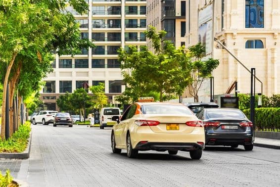 Coches en la carretera de Dubái, un taxi en primer plano, casas detrás.
