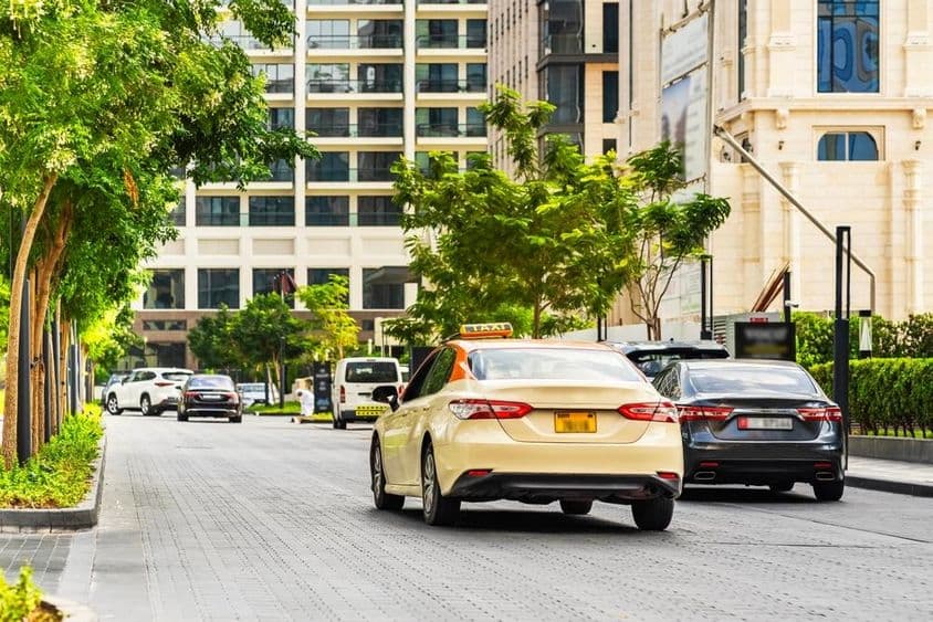 Coches en la carretera de Dubái, un taxi en primer plano, casas detrás.