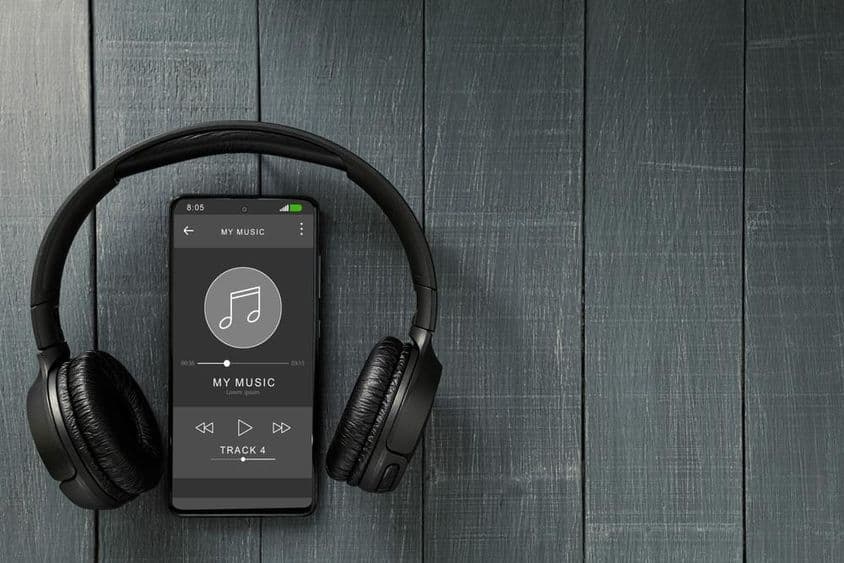 Reproducción de música en un teléfono, con auriculares al lado.