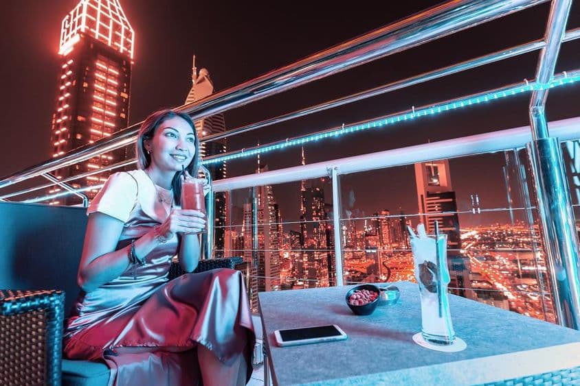 Mujer joven bebiendo cóctel en terraza de bar en azotea de Dubái.