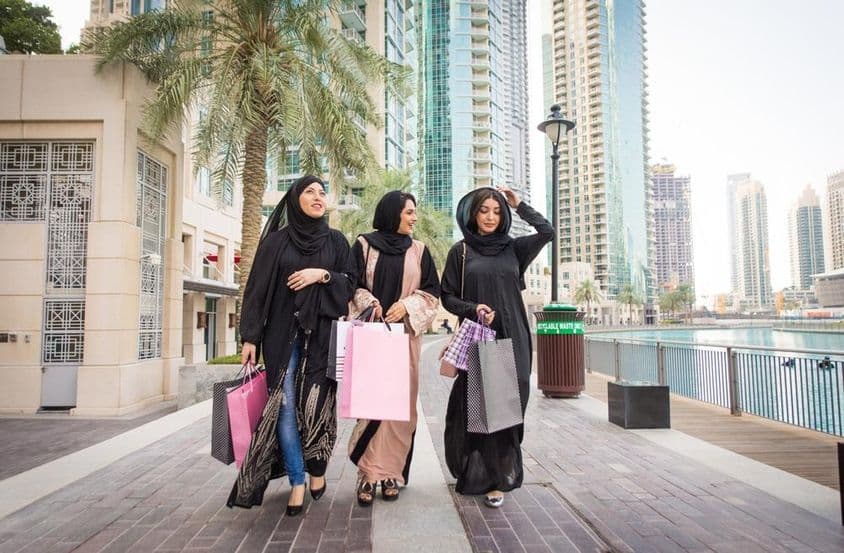 3 mujeres emiratíes caminando con bolsas de compras después de comprar, con rascacielos de fondo.