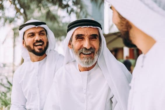 Un anciano emiratí conversando con dos personas más jóvenes.