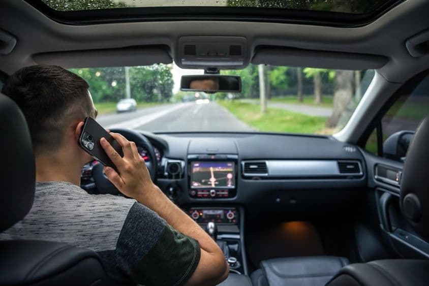 Joven usando su teléfono mientras conduce un coche.