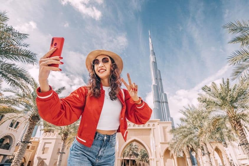 Joven mujer, en una blusa roja, tomándose una selfie con el Burj Khalifa al fondo.