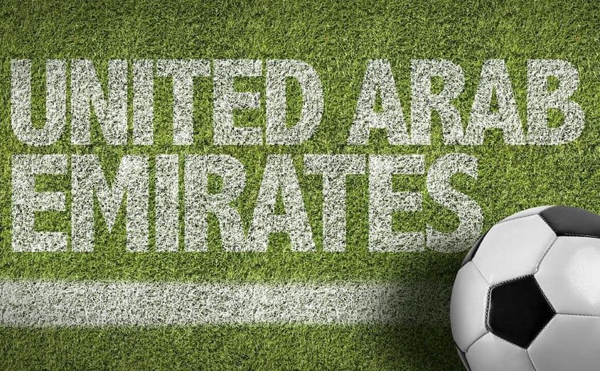 Inscripción 'EAU' pintada en el césped con un balón de fútbol.