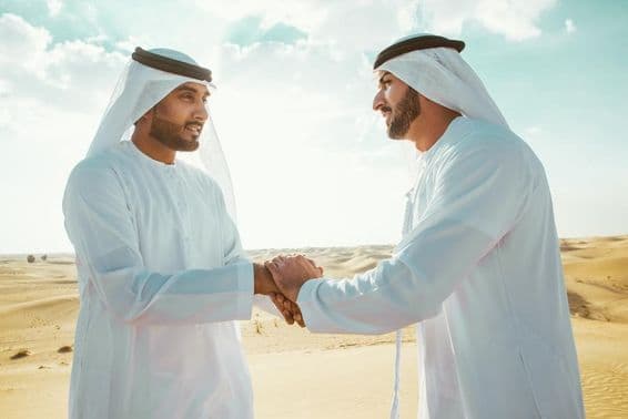 Dos hombres árabes dándose la mano en el desierto.
