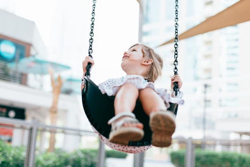 Niña pequeña feliz columpiándose en el patio del jardín de infantes.