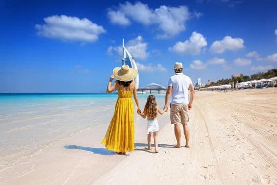 Una familia caminando por una playa de Dubái con el Burj al Arab al fondo.