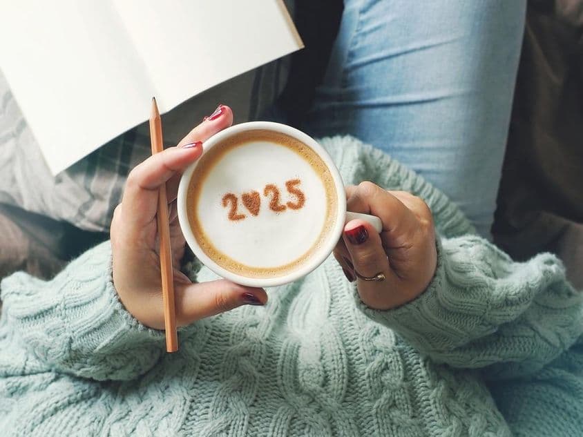 Una taza de café sostenida en la mano de una mujer, con 2025 escrito dentro.