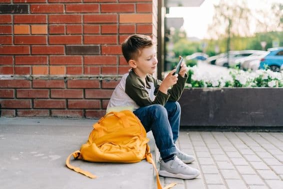 Niño usando un teléfono en los escalones de la escuela.