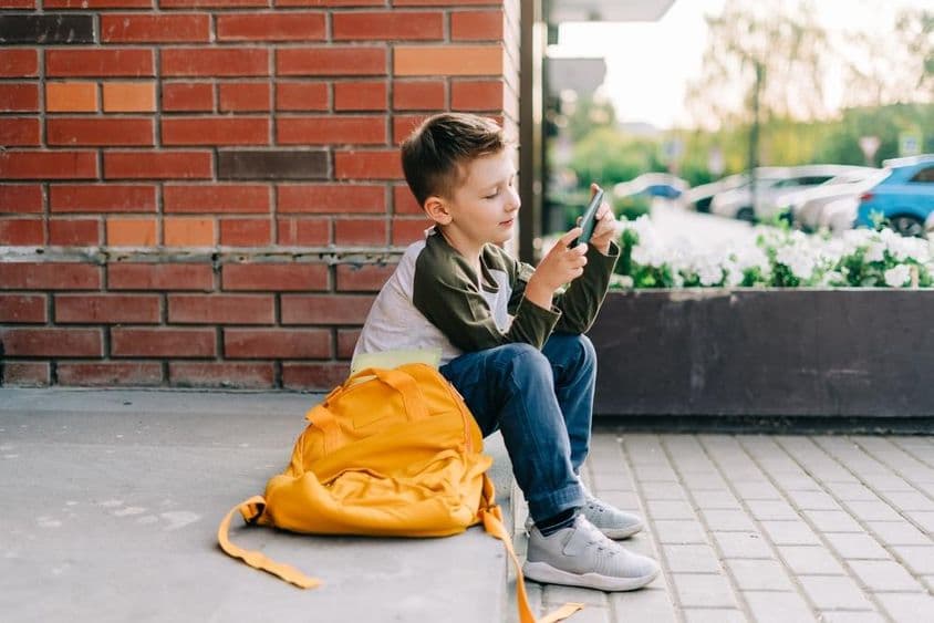 Niño usando un teléfono en los escalones de la escuela.