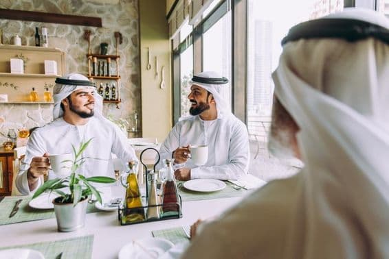Tres empresarios bebiendo té en Dubái, vistiendo atuendos tradicionales Emiratíes.