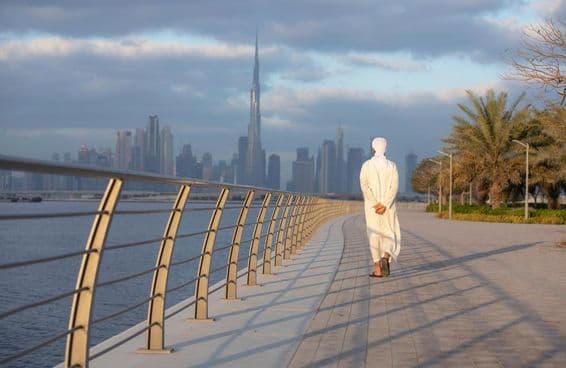 Hombre emiratí caminando por una acera con Burj Khalifa al fondo.