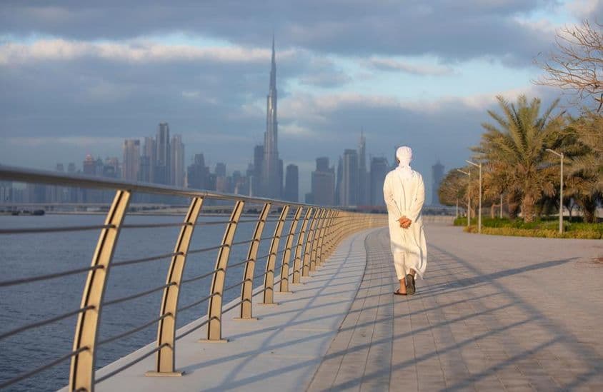 Hombre emiratí caminando por una acera con Burj Khalifa al fondo.