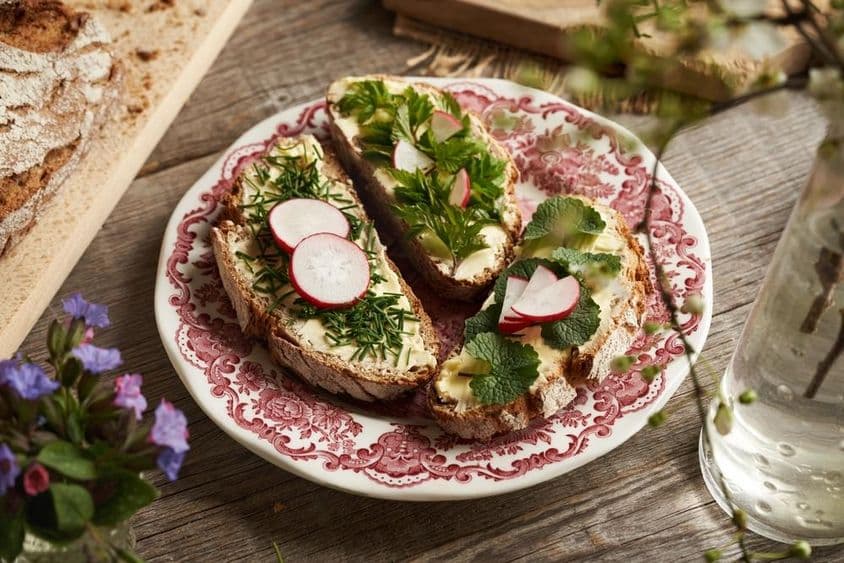 Plantas comestibles - cebollino, mostaza de ajo y grosellas sobre rebanadas de masa fermentada con mantequilla.