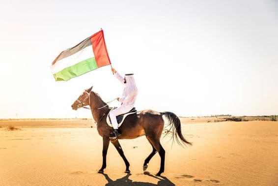 Hombre de Oriente Medio con ropa tradicional emiratí montando un caballo árabe en el desierto de Dubái.