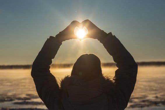 Mujer formando corazones con sus manos al aire libre en un atardecer helado.