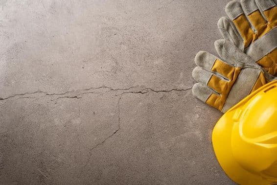 Tiempo de descanso, casco amarillo y guantes de trabajo colocados sobre una superficie de concreto agrietada.