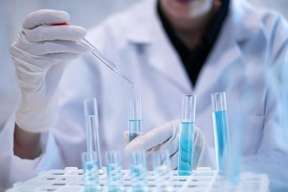 Científico pipeteando líquido azul en un tubo de ensayo en un laboratorio.