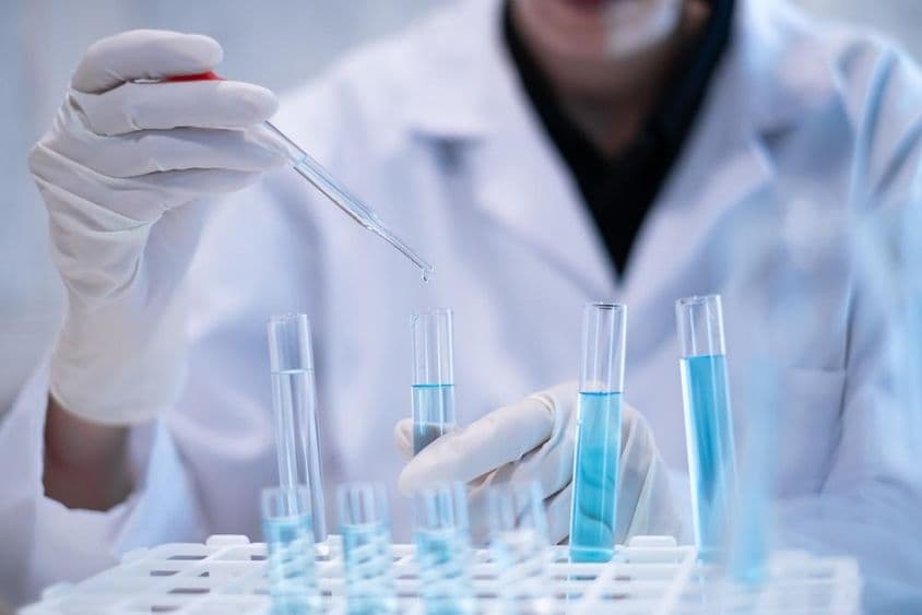 Científico pipeteando líquido azul en un tubo de ensayo en un laboratorio.