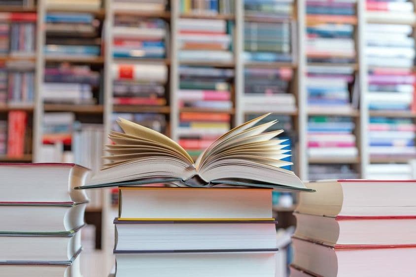 Libro abierto sobre una pila de libros frente a un estante.