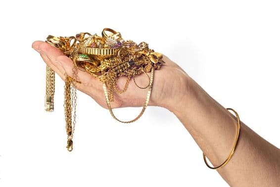Mano de mujer sosteniendo un montón de joyas de oro y usando una pulsera.