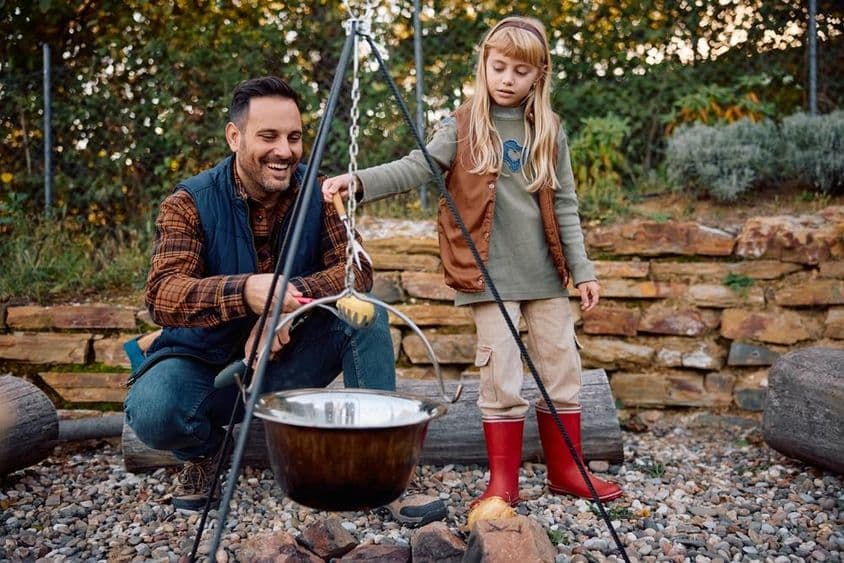 Niña ayuda a su padre a cocinar en una fogata en la naturaleza durante el otoño.