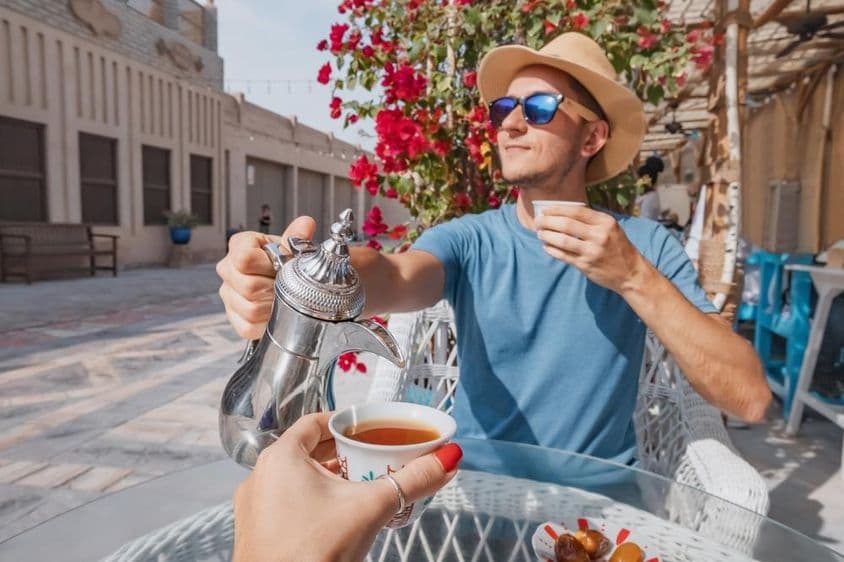 Un hombre en Dubái descansando en un café árabe, vertiendo café aromático de una cafetera dallah.