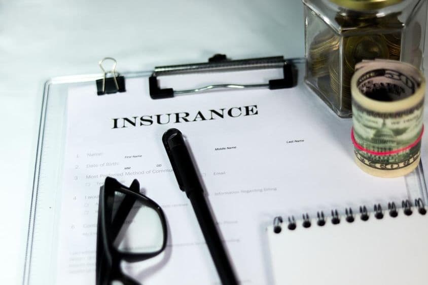 Formulario de seguro con caja de monedas, paquete de dólares, bolígrafo y gafas.