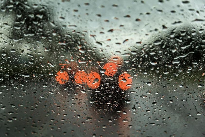 Día lluvioso en Dubái con luces de coche visibles a la distancia, visto a través de una ventana de coche con gotas de lluvia.