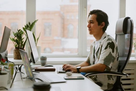 Joven programador sentado en un escritorio, codificando en una computadora en una oficina luminosa.