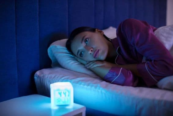 Mujer triste sin poder dormir, acostada en la cama, mirando al vacío, sufriendo de insomnio.