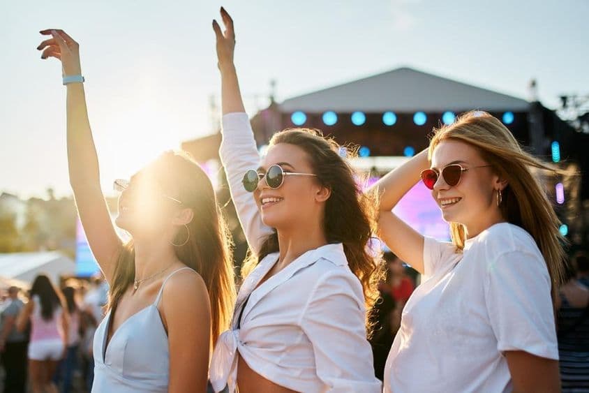 Chicas con vestidos de verano disfrutando de un concierto, celebrando con manos levantadas.