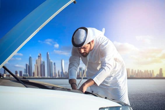 Un hombre árabe inspeccionando su coche, capó abierto.