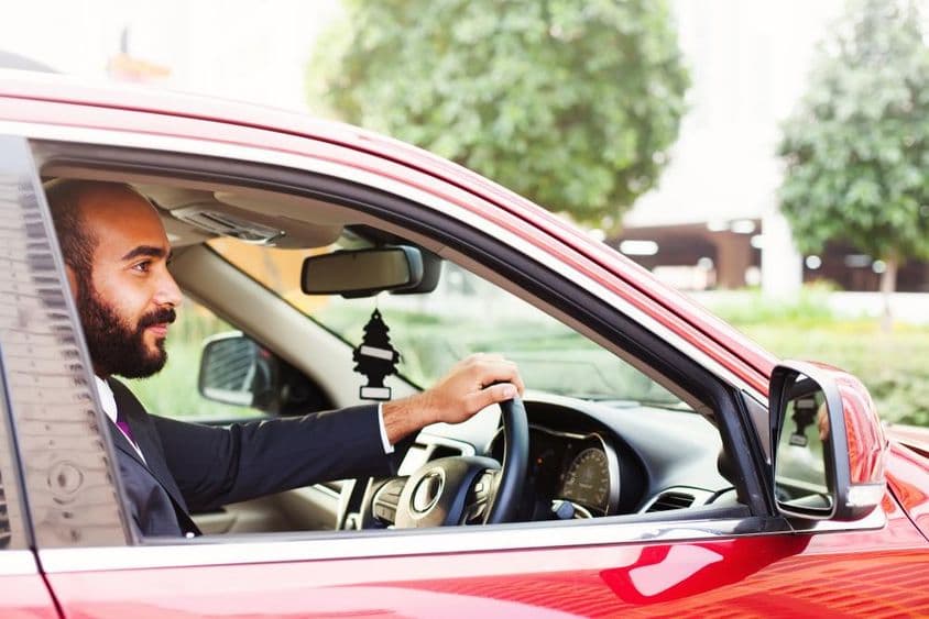 Joven empresario conduciendo un coche de alquiler rojo.