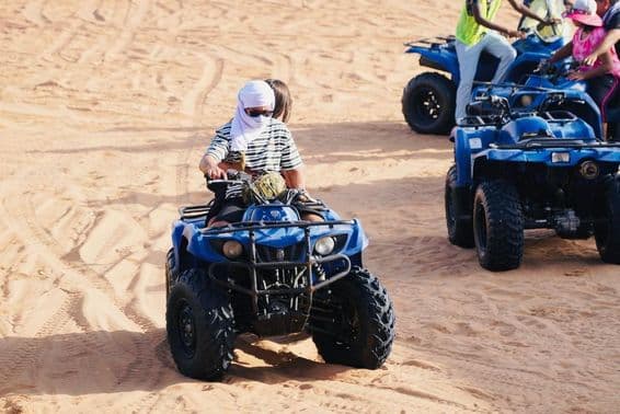 Joven pareja montando un quad en el desierto de Dubái.