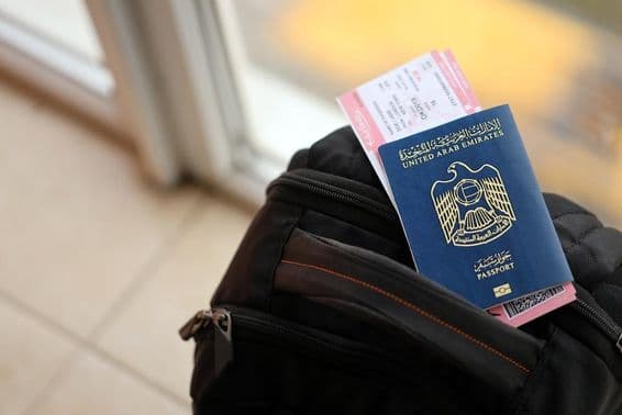 Pasaporte azul de los Emiratos Árabes Unidos con boletos de vuelo en una mochila en primer plano.