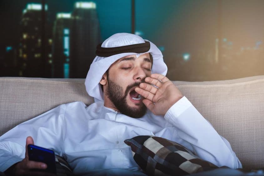 Hombre árabe bostezando mientras ve televisión.
