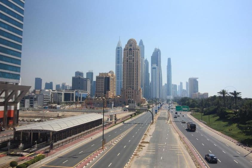 Vista de calle en Dubai con rascacielos y tranvía al fondo.